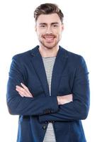 Confident young man. Handsome young man keeping arms crossed and smiling while standing against white background photo