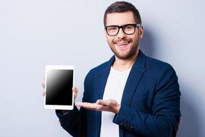 copie el espacio en su tableta. un joven alegre que muestra una tableta digital y sonríe mientras se enfrenta a un fondo gris foto