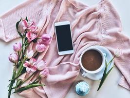 Beauty and tender. High angle shot of sweater, flowers, smart phone, cup of coffee, and cupcake lying against white background photo