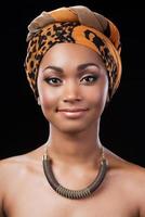 belleza cándida. retrato de una hermosa mujer africana con pañuelo en la cabeza y sonriendo mientras mira la cámara y se enfrenta a un fondo negro foto