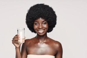 Portrait of beautiful young African woman holding glass with water and smiling photo