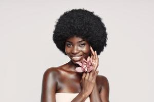 Portrait of beautiful young African woman holding flower near face and smiling photo