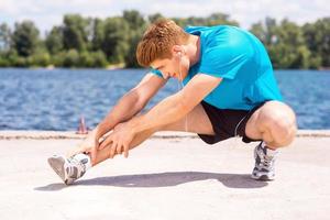 Warming up. Handsome young man doing stretching exercises while standing outdoors photo