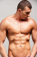 Strength and masculinity. Confident young muscular man posing while standing against grey background photo