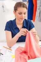 Confident tailor sewing. Beautiful young woman sewing while sitting at her working place photo