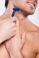 Shaving with bad razor. Cropped image of handsome young man shaving and grimacing while standing isolated on grey background photo