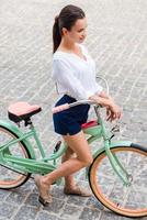 Ready to ride. Top view of attractive young smiling woman walking with bicycle photo