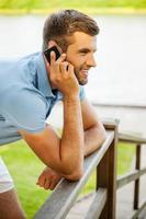 Good talk. Side view of handsome young man talking on the mobile phone and smiling while standing outdoors photo