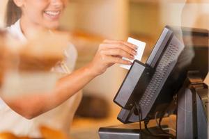 Cashier at work. Beautiful young female cashier swipes a plastic card through a machine photo