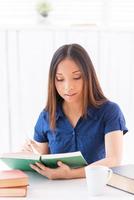 Beautiful bookworm. Beautiful young Asian woman reading a book while sitting at the table photo