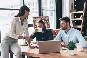 Successful team. Young modern colleagues in smart casual wear working together and smiling while spending time in the office photo