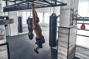 Working hard. Full length top view of young African man doing pull-ups while exercising in the gym photo