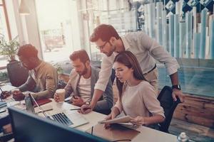 Group of young modern people in smart casual wear communicating and using modern technologies while working in the office photo
