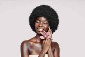 retrato de una hermosa joven africana sosteniendo una flor cerca de la cara y sonriendo foto