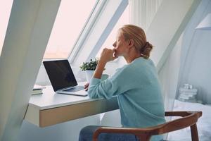 Beautiful young woman using laptop while working at home photo