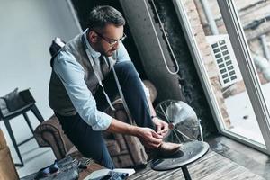 Another working day. Handsome young man in suit tying his shoe while standing in the workshop photo