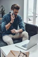 In touch with clients. Thoughtful young modern man talking on smart phone while sitting at his working place photo