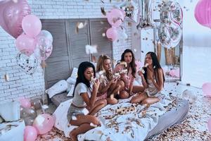 Unhealthy so what Top view of four beautiful young women in pajamas eating cake while having a slumber party in the bedroom with balloons all over the place photo