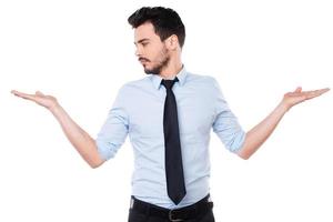 Making his choice. Handsome young man in shirt and tie making his choice while looking at one of his palms and standing against white background photo