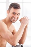 Feeling confident. Side view of handsome young muscular man sitting on the chair and smiling at camera photo