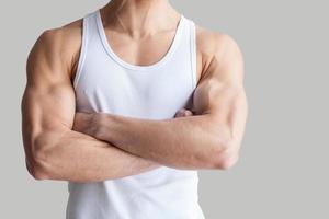 Strong and healthy body. Cropped image of muscular man keeping arms crossed while standing isolated on grey background photo