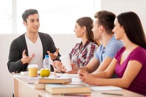 Cheerful students. Four cheerful students talking to each other while sitting at the desk photo