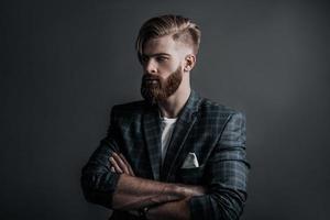 Confidence and charisma. Attractive young man keeping arms crossed and looking away while standing against grey background photo