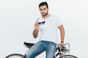 Stylish handsome. Handsome young Indian man leaning at his retro styled bicycle and looking at camera while standing against white background photo