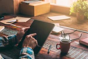 Opening the world with single touch. Close-up image of man holding digital tablet with copy space while sitting at the rustic wooden table photo