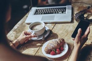 Always in touch. Close up rear view of woman using smart phone while having breakfast at home photo