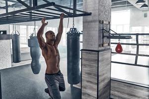 Just do it. Handsome young African man doing pull-ups while exercising in the gym photo