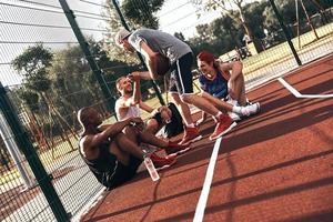 gracias por jugar. grupo de jóvenes con ropa deportiva sonriendo mientras se sientan en el campo de baloncesto al aire libre foto