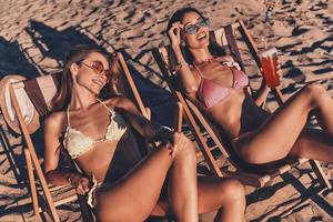 totalmente despreocupado. vista superior de atractivas mujeres jóvenes sonriendo y tomando el sol mientras descansan en sillas al aire libre en la playa foto