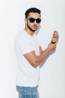 Confident in his style. Side view of handsome young Indian man adjusting his bracelet and looking at camera while standing against white background photo