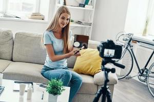 Beautiful young woman smiling and applying make-up while making social media video at home photo