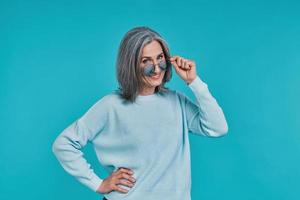 Mature beautiful woman looking at camera and smiling while standing against blue background photo