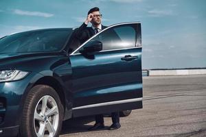 hombre de negocios elegante. apuesto joven hombre de negocios entrando en su auto mientras está parado afuera foto