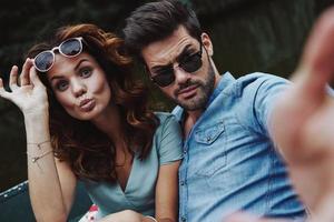 No cares and no rules. Self portrait of beautiful young couple looking at camera while sitting in the boat outdoors photo