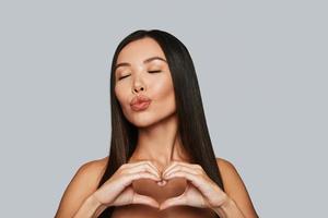 With love. Beautiful young Asian woman gesturing and puckering while standing against grey background photo