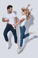 Crazy couple. Full length of beautiful young couple smiling while jumping against grey background photo