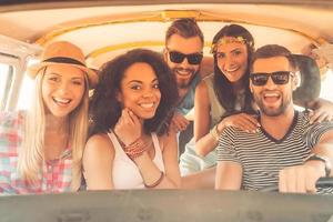 Life is better when friends are near. Group of joyful young people smiling at camera while sitting inside of minivan together photo