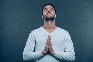 Man praying. Studio shot of handsome young man praying while holding hands clasped and keeping eyes closed photo