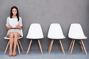 Waiting for interview. Confident young businesswoman holding paper while sitting on chair against grey background photo