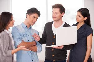 Discussing project together. Group of young people discussing something while one man holding laptop photo