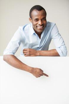 hermoso espacio de copia señalador. hombre africano alegre con camisa azul apoyado en el espacio de la copia y apuntándolo mientras está de pie contra el fondo gris foto