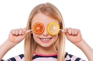 divirtiéndose con dulces. niña alegre que cubre los ojos con piruletas y sonriendo mientras está aislada en blanco foto