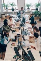 Top view of young modern people in smart casual wear communicating and using modern technologies while working in the office photo