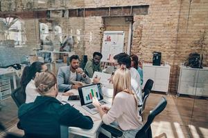 Group of young modern people in smart casual wear using modern technologies while working in the board room photo