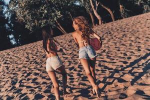 sentirse libre y feliz. dos atractivas mujeres jóvenes en pantalones cortos y trajes de baño sonriendo mientras corren en la playa foto