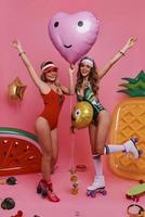 Simply happy. Full length of two attractive young women in swimwear smiling and gesturing while posing against pink background photo